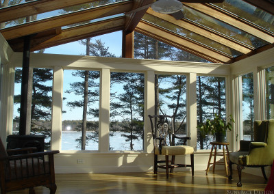 A gorgeous lakeside sunroom with a mahogany framed glass ceiling offers panoramic views of the surrounding natural environment