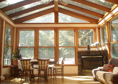 A rustic sunroom with a marble fireplace and dining area is illuminated by bright rays of sunlight