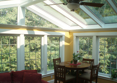 A bright and airy sunroom features a circular breakfast table beside tall windows and an entertainment space