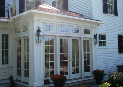 A view of a custom glass enclosure showing off tall windows, a glass roof lantern, French doors, elegant lighting fixtures, and a tiled patio