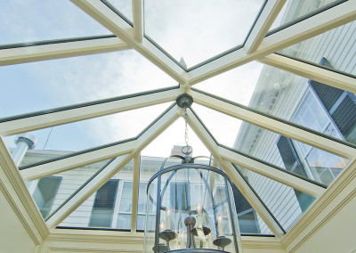 A gorgeous lighting fixture is suspended from the center of a beautiful orangery glass roof with angular framing elements