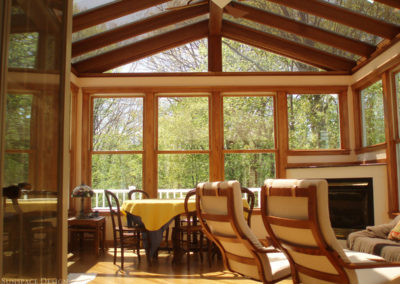 The white railings of a wraparound deck are visible through the tall windows of a thermally efficient, traditional sunroom in Newton, Massachusetts