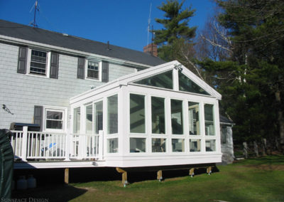 An exterior view of a raised sunroom connected to both the back deck grilling area and kitchen of a residence