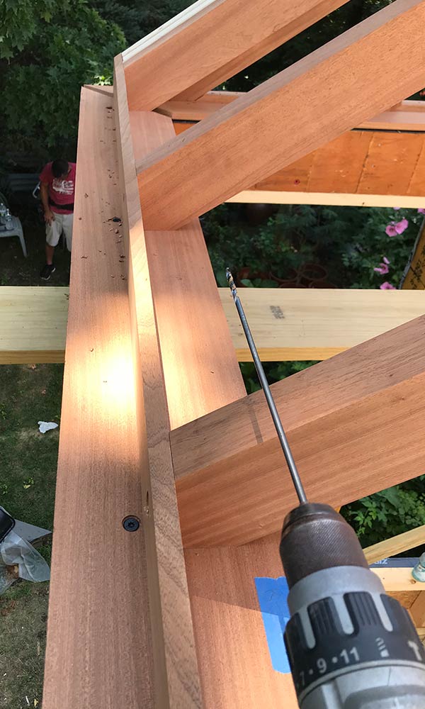 A look at a drill being used to attach mahogany rafters and a sill to the conventionally constructed addition's frame before fasteners are concealed